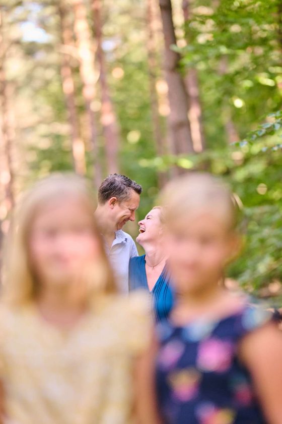 Couple smiling in the forest with children in the foreground.