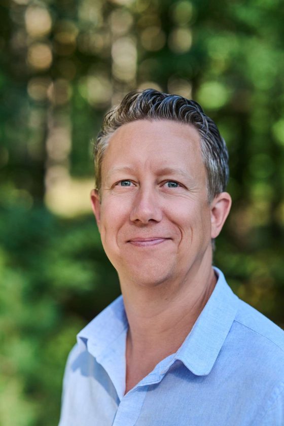 Smiling person in front of a blurred forest background.