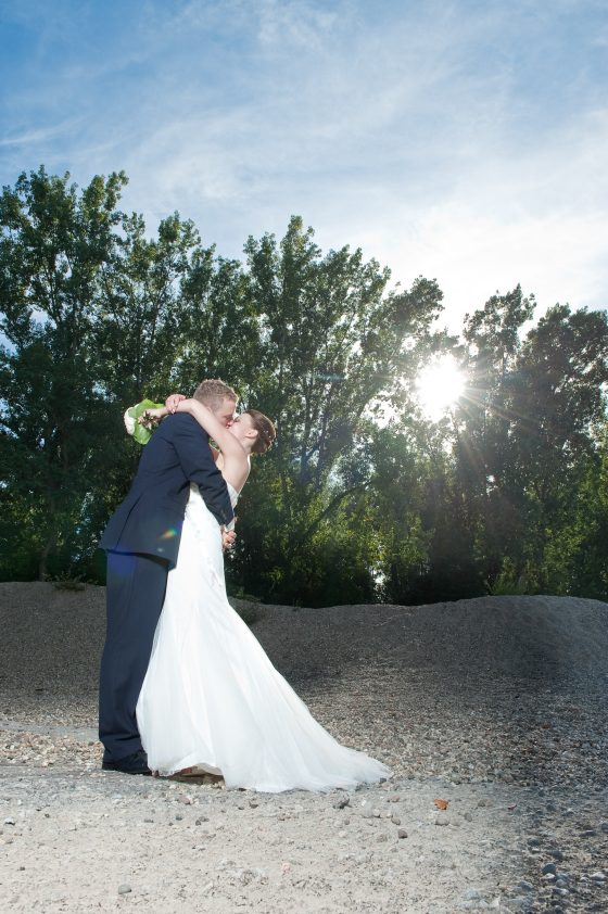 Bride and groom kissing in front of a sunny forest background.