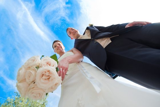 Bridal couple with a bouquet of flowers in front of a blue sky.