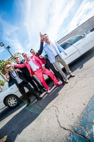 Gruppe Männer vor weißer Limousine feiernd