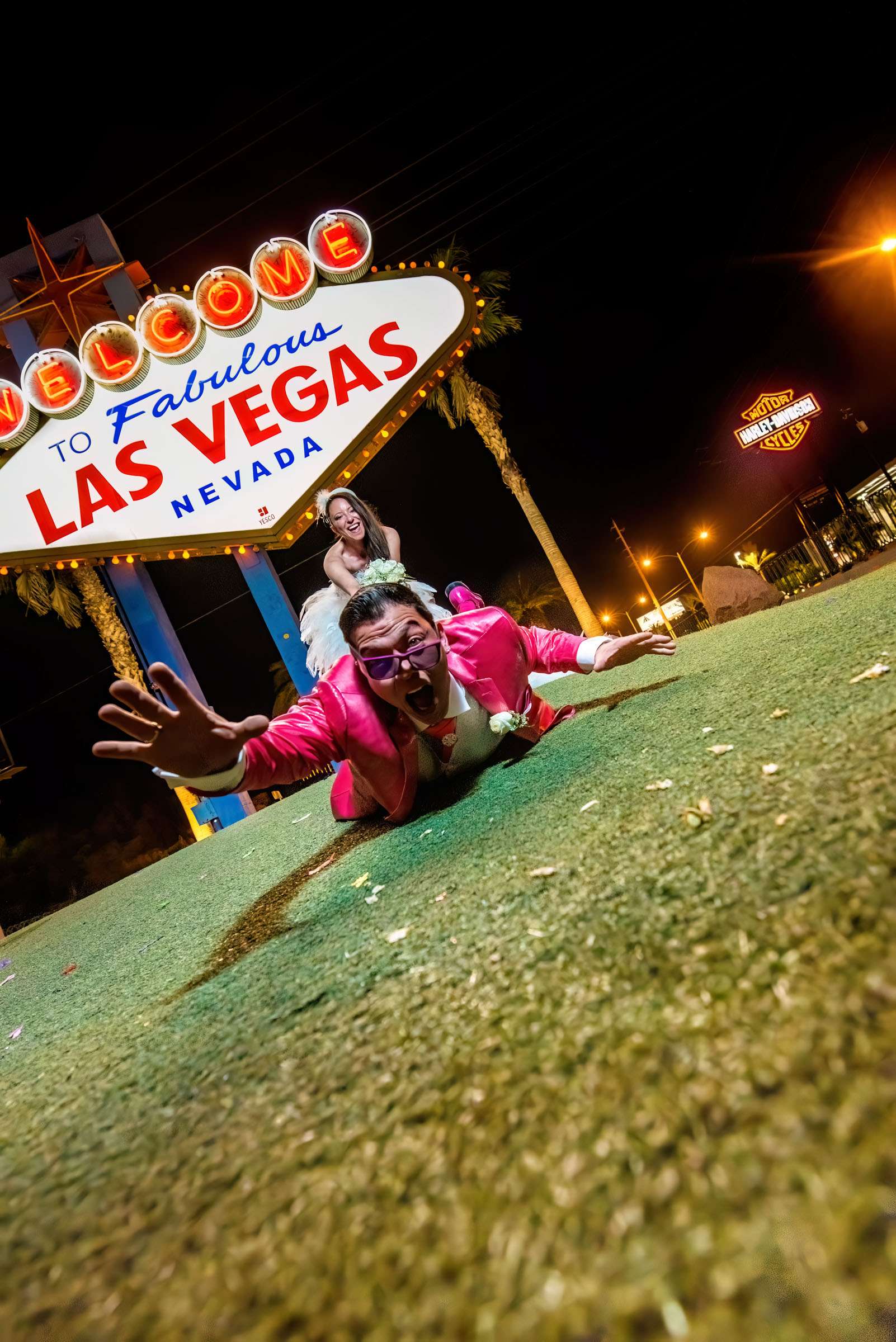 Wedding couples pose in front of Las Vegas sign at night.