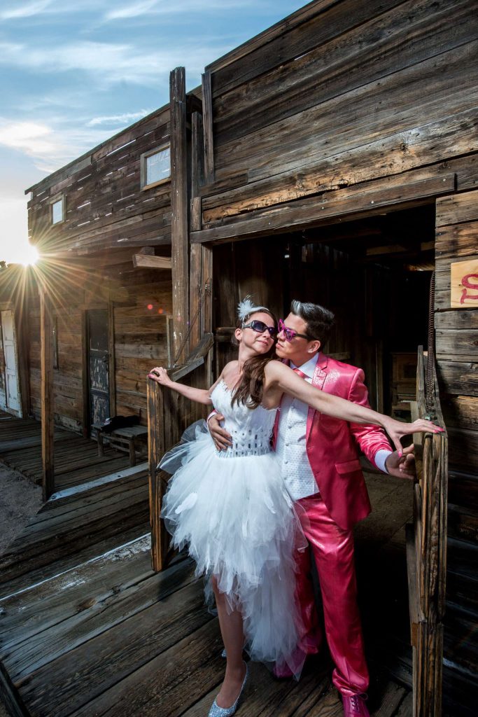 Couple posing in colorful clothes in front of a wooden hut.